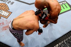 Na posição de John Dodson (bermuda cinza) acima, um lutador poderá ser golpeado na cabeça mesmo se tocar o chão com uma mão. Foto: Josh Hedges/UFC.com